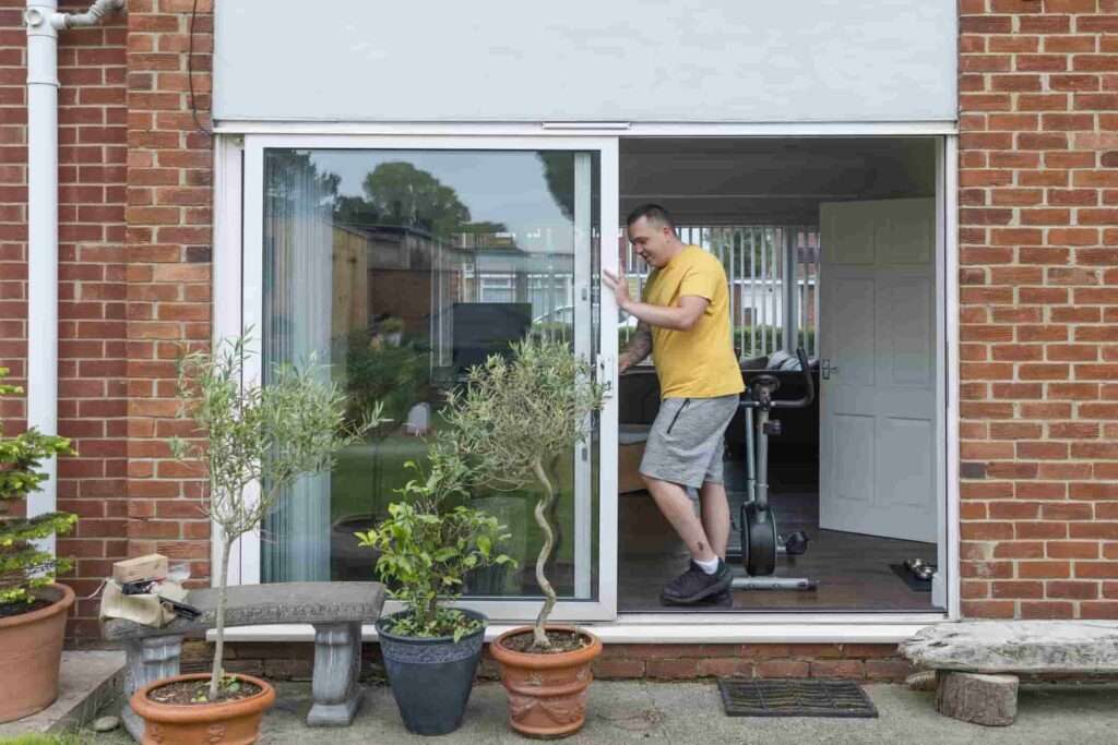 A man stands in front of a sliding glass door in San Jose, looking out into the outdoors.
