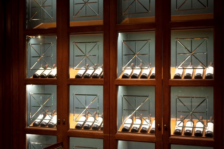 Glass wine cellar with wooden racks holding assorted wine bottles in San Jose