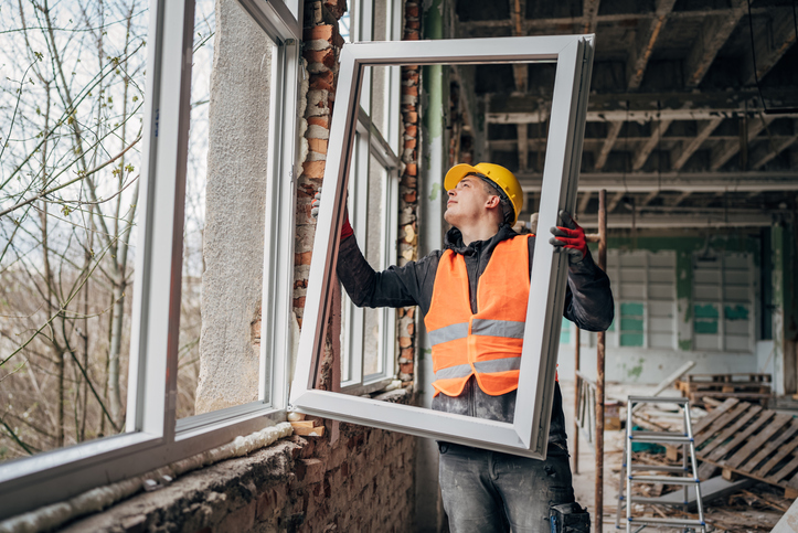 Construction worker installing new window frame inside building in San Jose, CA.